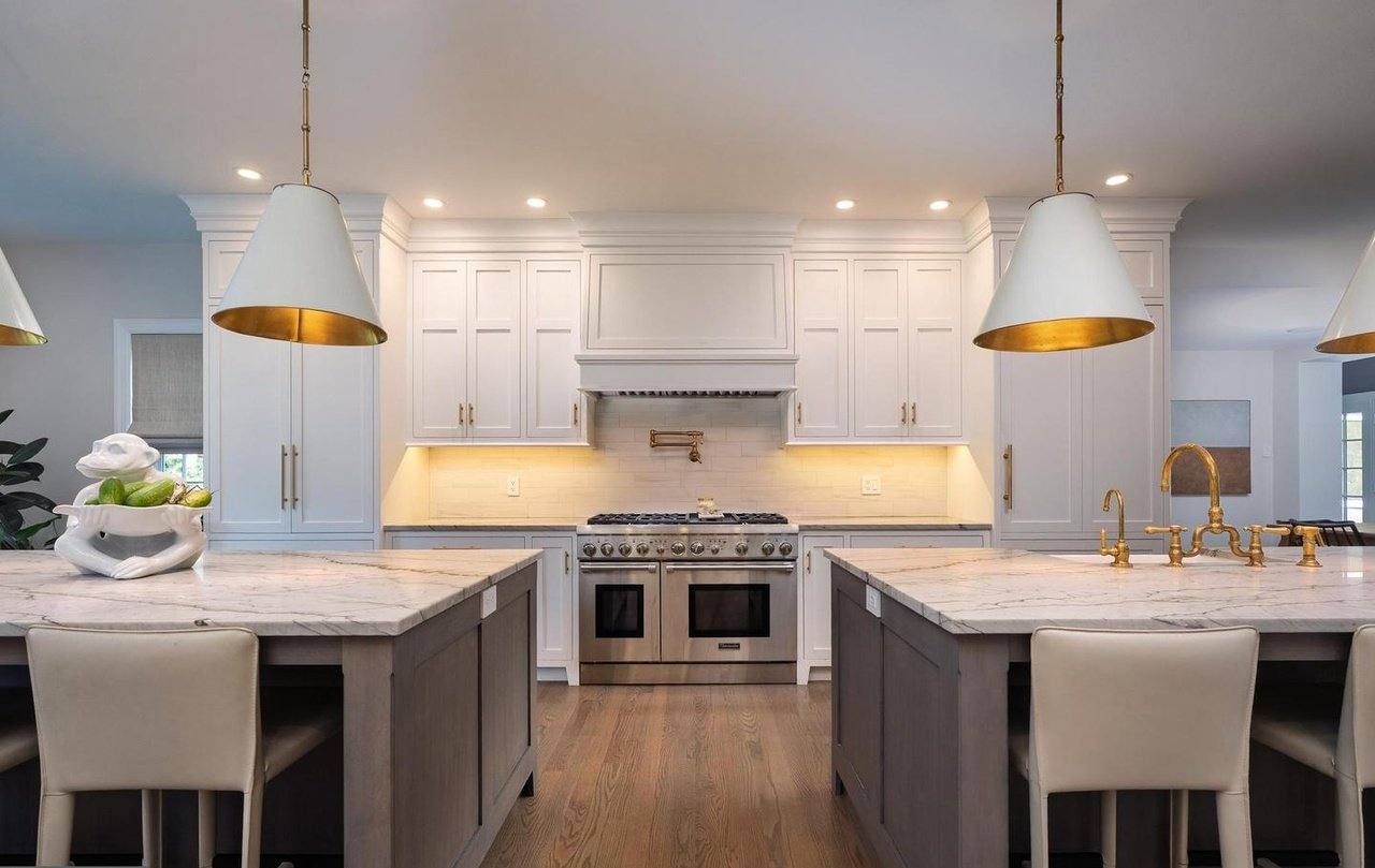 Kitchen with white custom cabinetry, a large marble island with gold pendants, and a professional range